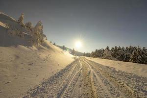 landskap med Sol, snö och bil spår på de väg i de vinter- i de berg. de begrepp av vinter- resa förbi bil. foto