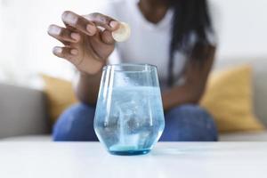 närbild av en ung kvinna dropp ett bubblande antacidum i en glas av vatten. ung kvinna knappast sätta en löslig piller med en medicin för smärta eller en baksmälla i en glas av vatten foto