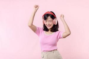 leende Söt modell person lyssna musik låt och njut av dansa med trådlös hörlurar uppkopplad audio radio ljud. positiv roligt exits glad ungdom kvinna kvinna sjunga på rosa isolerat bakgrund studio foto