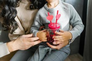 en glas smoothie råna med två rör med hjärtan i de händer av en ung son. hjärtans dag i de familj foto