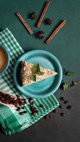 topp se av utsökt napoleon kaka med grädde på en turkos tallrik dekorerad med en kvist av mynta på en grön bakgrund. en kopp av varm kaffe, kanel pinne, badyan, kaffe bönor på en grön backgroun foto