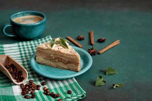 färsk utsökt kaka napoleon med grädde på en grön bakgrund. en kopp av varm kaffe, kanel pinne, badyan, kaffe bönor på en grön bakgrund. kopia Plats foto