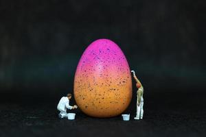 miniatyr människor målar påskägg för påskdag på en svart bakgrund foto