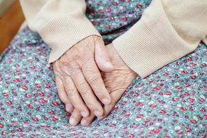 asiatisk äldre äldre kvinna patient sitter på sängen på sjukhus, närbild på hennes hand. foto