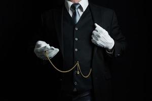 porträtt av butler i mörk kostym och vit handskar innehav guld ficka Kolla på. årgång stil och professionell artighet. foto