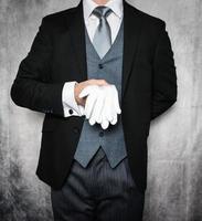 porträtt av butler eller hotell concierge i mörk kostym och vit handskar ivrig till vara av service. begrepp av elegant gästfrihet och professionell artighet. foto