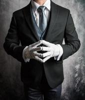 porträtt av butler eller hotell concierge i mörk kostym och vit handskar ivrig till vara av service. professionell artighet och gästfrihet. foto