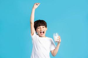 porträtt av asiatisk pojke innehav kopp av mjölk, isolerat på blå bakgrund foto