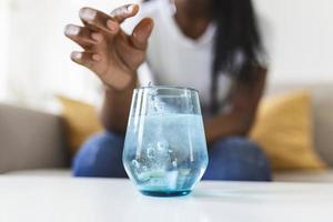 närbild av en ung kvinna dropp ett bubblande antacidum i en glas av vatten. ung kvinna knappast sätta en löslig piller med en medicin för smärta eller en baksmälla i en glas av vatten foto