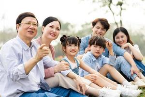 bild av ett asiatisk familj Sammanträde tillsammans på de gräs på de parkera foto