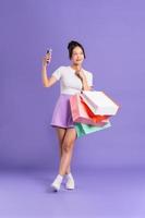 ung asiatisk kvinna innehav handla väska på lila bakgrund foto