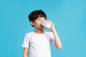 porträtt av asiatisk pojke innehav kopp av mjölk, isolerat på blå bakgrund foto