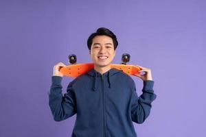 bild av ung asiatisk man spelar skateboard på lila bakgrund foto