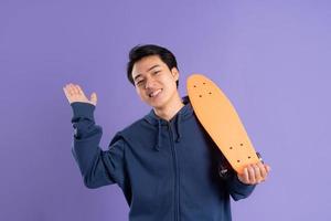 bild av ung asiatisk man spelar skateboard på lila bakgrund foto