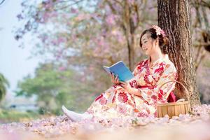 lady i traditionell kimono klänning läsning bok på körsbär blomma träd i vår festival. foto