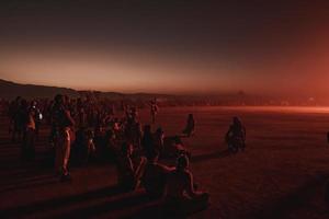 människor gående mot solnedgång på en festival i de öken- på de brinnande man festival. foto