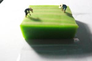 en stänga upp av en miniatyr- figur av en jordbrukare vem är jordbruk på en grön lager kaka tycka om en ris fält. jordbrukare jordbruk begrepp. foto