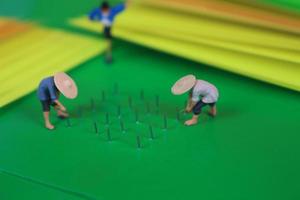 miniatyr- figur av jordbrukare växande gröda i de form av häftklamrar på grön papper. begrepp av lantbruk Foto. foto