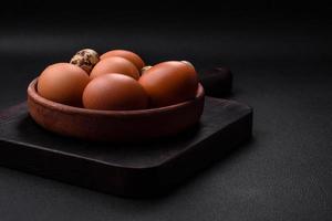 rå kyckling och vaktel ägg i en brun keramisk skål på en mörk betong bakgrund foto
