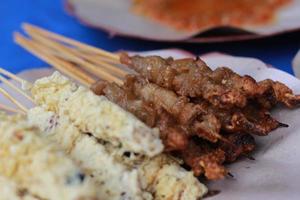Foto av kyckling satay överdragen med friterad ägg och kyckling inälvor satay eras med röd chili sås. indonesiska mat kallad sate taichan. mat begrepp Foto.