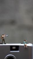 en miniatyr- figur tar bild med en kamera mot en verklig kamera i de bakgrund. foto