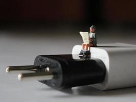 en stänga upp av en miniatyr- figur av en person läsning ovan en cell telefon laddare. foto