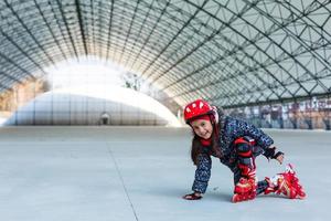 liten söt Lycklig flicka rullskridskor i en stor hangar foto