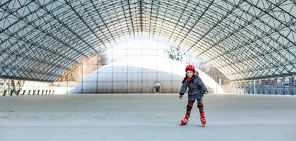 liten söt Lycklig flicka rullskridskor i en stor hangar foto