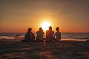 grupp av fem Lycklig människor sitter på bakgrund av tömma solnedgång strand. resa eller hav semester begrepp foto