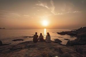 grupp av fem Lycklig människor sitter på bakgrund av tömma solnedgång strand. resa eller hav semester begrepp foto