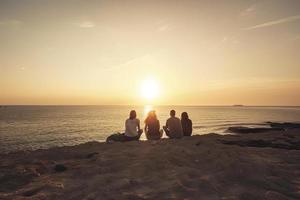 grupp av fem Lycklig människor sitter på bakgrund av tömma solnedgång strand. resa eller hav semester begrepp foto