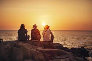 grupp av fem Lycklig människor sitter på bakgrund av tömma solnedgång strand. resa eller hav semester begrepp foto