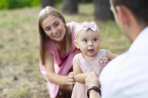 Make, fru och deras liten dotter för en promenad i de parkera. Lycklig pappa och mamma med ett år gammal bebis flicka. ung familj. foto