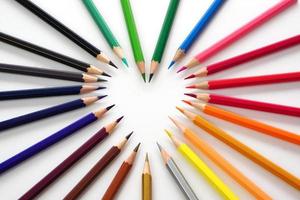 topp se av färgad pennor eller pastell anordnad i en hjärta form på vit bakgrund. inlärning, studie och presentation begrepp. foto