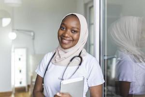 ung kvinna muslim afrikansk klinikern läkare i scrubs använder sig av pekplatta medan kommunicerar med patienter uppkopplad foto