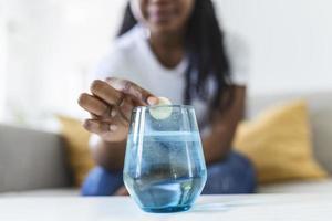 närbild av en ung kvinna dropp ett bubblande antacidum i en glas av vatten. ung kvinna knappast sätta en löslig piller med en medicin för smärta eller en baksmälla i en glas av vatten foto