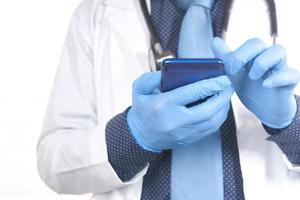 läkarens händer i skyddshandskar med en smartphone foto