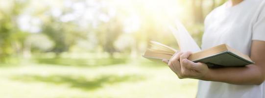 läs- och kunskapskoncept, hand som håller boken på mjuk grön parkbannerbakgrund