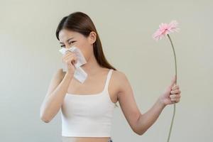 allergisk rinit symptom av odör pollen blommande, porträtt asiatisk ung kvinna hand i nysa, blåser rinnande näsa efter lukt, stinkande från blomma blomma, innehav bort rosa flora på vit bakgrund. foto