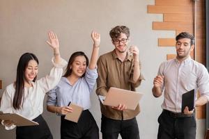 heja på upp, förvånad företag människor grupp, lagarbete av ung asiatisk, kaukasisk har kul, glad i arbetsplats efter projekt är gjort, vinn medan konferens med partners på laptop.firar Framgång begrepp. foto