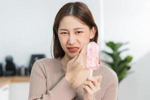 hälsa asiatisk ung kvinna rörande kind, uttryck, lidande från tandvärk, förfall eller känslighet hålighet molar- tand, tänder eller inflammation äta kall is grädde på Hem. känslig tänder människor. foto