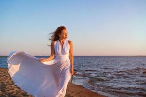 ung vuxen kvinna i en vit klänning på de strand foto