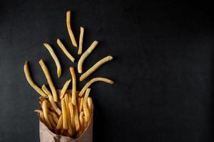 heta krispiga pommes frites i en papperspåse på svart bakgrund. god amerikansk snabbmat. foto