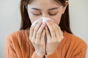 sjuk, coronavirus covid asiatisk ung kvinna, flicka ha en feber, influensa, hand i använda sig av vävnader papper nysning näsa, rinnande och hosta, stående på isolerat bakgrund. hälsa vård till sjukdom influensa säsong- foto