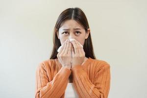 sjuk, coronavirus covid asiatisk ung kvinna, flicka ha en feber, influensa, hand i använda sig av vävnader papper nysning näsa, rinnande och hosta, stående på isolerat bakgrund. hälsa vård till sjukdom influensa säsong- foto