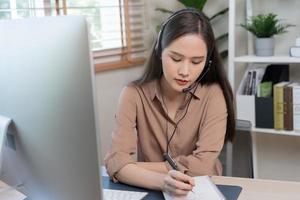 video ringa upp, möte konferens via kamera, Lycklig Söt asiatisk ung kvinna, flicka Sammanträde, ha på sig trådlös hörlurar studie uppkopplad, använder sig av bärbar dator dator, frilansare working.technology, social distans. foto