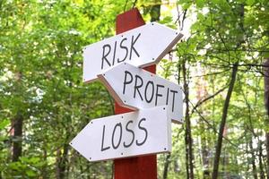 risk, vinst, förlust - trä- vägvisare med tre pilar, skog i bakgrund foto
