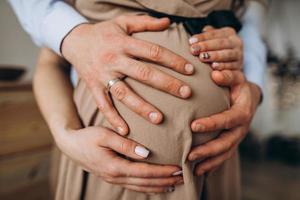 mannens händer omfamning en mage av de gravid kvinna foto