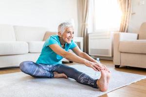 senior kvinna håller på med uppvärmning träna på Hem. kondition kvinna håller på med sträcka övning stretching henne ben, quadriceps .äldre kvinna levande ett aktiva livsstil. foto