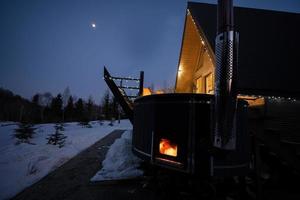 trä- tunna varm badkar i de terrass av de stuga på vinter- natt. scandinavian badkar med en öppen spis till bränna trä och värme vatten. foto